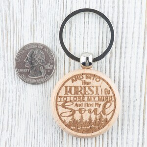 Op de afbeelding: Houten sleutelhanger met een zilveren ring. De sleutelhanger heeft een gegraveerde quote die luidt: "En de bossen in ga ik om mijn verstand te verliezen en mijn ziel te vinden".