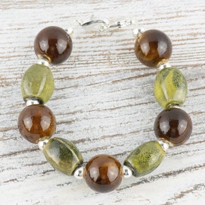 May include: A brown and green glass bead bracelet with a silver clasp. The bracelet has alternating round and oval beads.