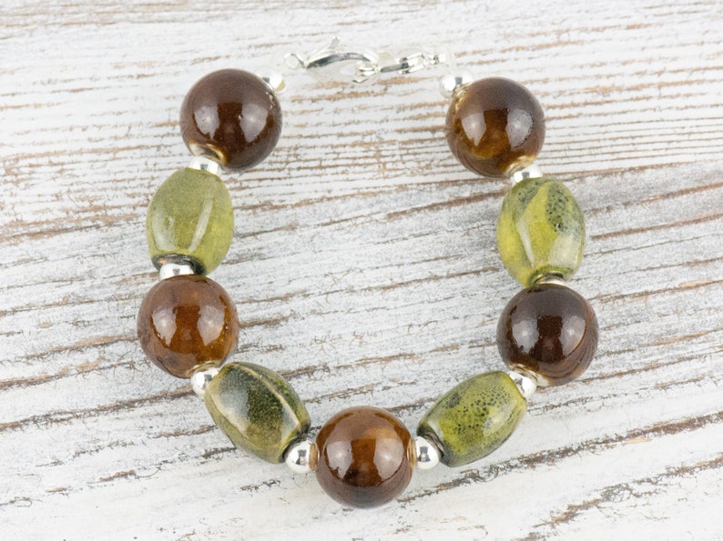 May include: A brown and green glass bead bracelet with a silver clasp. The bracelet has alternating round and oval beads.