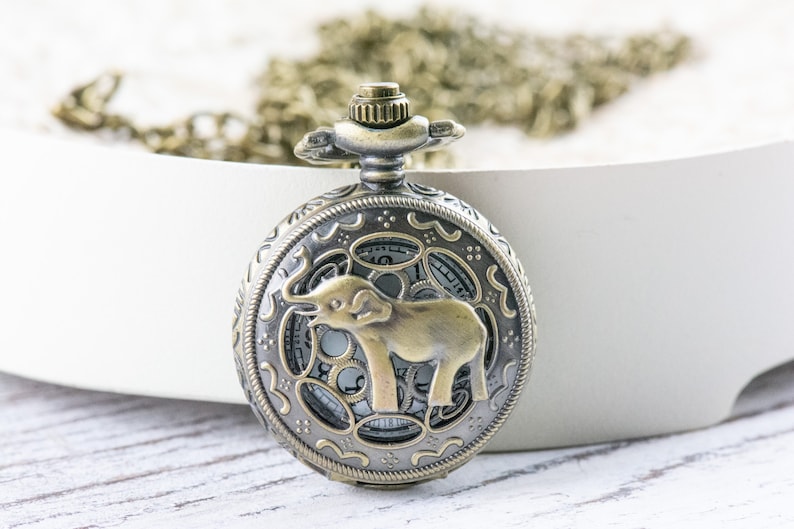 May include: A bronze pocket watch with an ornate design and an elephant silhouette on the face.