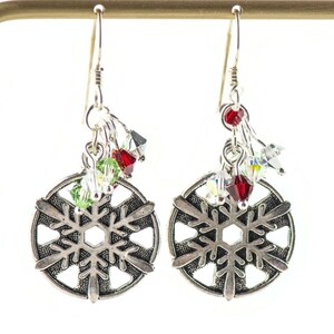 Puede incluir: Pendientes de copo de nieve de plata con detalles de cristal rojo, verde y transparente.