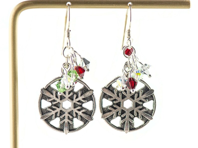 Puede incluir: Pendientes de copo de nieve de plata con detalles de cristal rojo, verde y transparente.