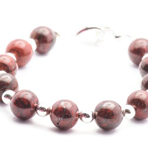 May include: A red and silver bracelet with round beads. The beads are made of a red stone with silver flecks.