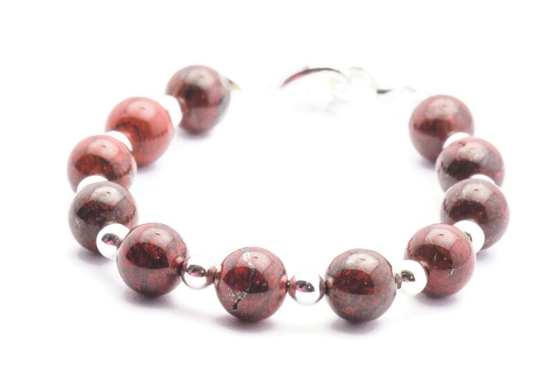 May include: A red and silver bracelet with round beads. The beads are made of a red stone with silver flecks.
