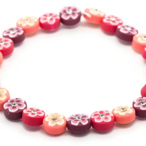 K&ouml;nnte beinhalten: Eine bunte Halskette aus runden Perlen mit Blumenmustern und Strasssteinen. Die Perlen sind in den Farben Rosa, Rot und Lila.