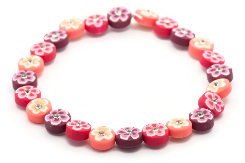K&ouml;nnte beinhalten: Eine bunte Halskette aus runden Perlen mit Blumenmustern und Strasssteinen. Die Perlen sind in den Farben Rosa, Rot und Lila.