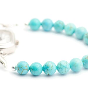 May include: A silver watch with a square face attached to a turquoise beaded bracelet.