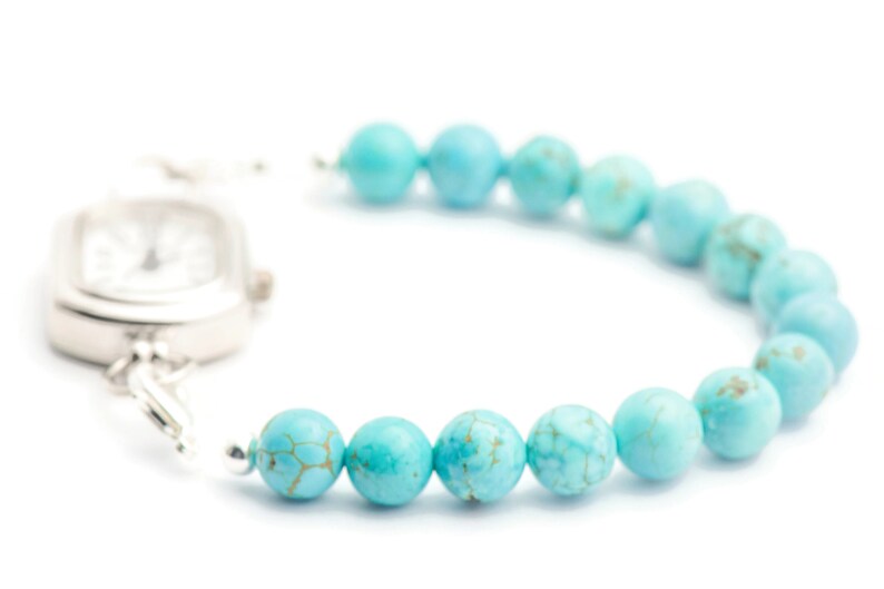 May include: A silver watch with a square face attached to a turquoise beaded bracelet.