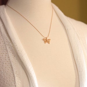 Peut inclure: Un collier avec un pendentif en forme de papillon dor&eacute; sur un mannequin blanc. Le collier est d&eacute;licat et pr&eacute;sente un motif de papillon d&eacute;taill&eacute;.