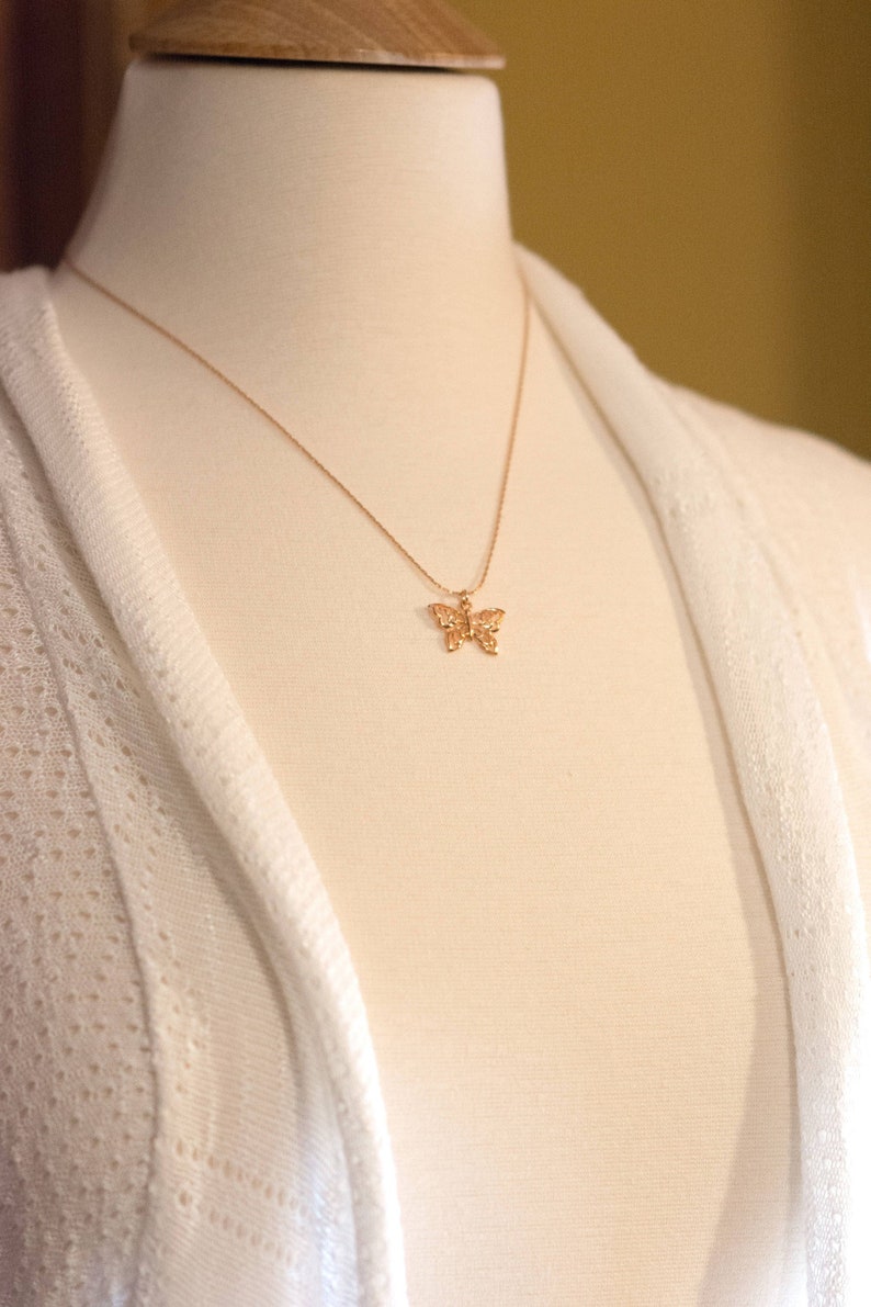 Peut inclure: Un collier avec un pendentif en forme de papillon dor&eacute; sur un mannequin blanc. Le collier est d&eacute;licat et pr&eacute;sente un motif de papillon d&eacute;taill&eacute;.