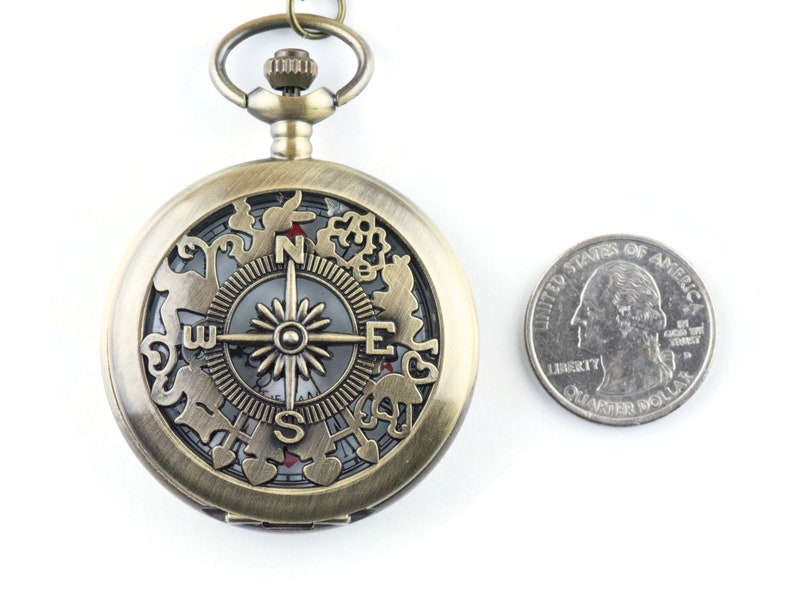 Op de afbeelding: Een bronzen zakhorloge met een kompasgezicht en een decoratief ontwerp rond de rand. Het horloge is ongeveer zo groot als een Nederlandse 2 euro munt.