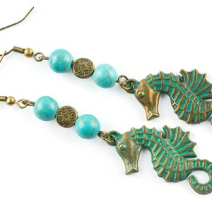 May include: A pair of turquoise and bronze earrings featuring seahorse charms and turquoise beads. The beads have a textured surface and the seahorse charms have a detailed design.
