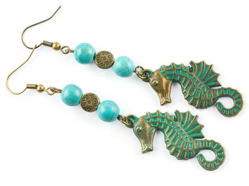 May include: A pair of turquoise and bronze earrings featuring seahorse charms and turquoise beads. The beads have a textured surface and the seahorse charms have a detailed design.