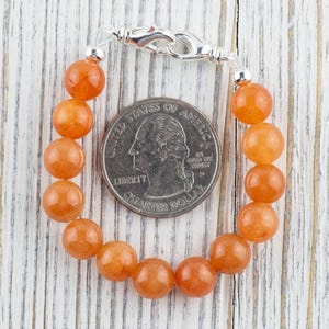 Op de afbeelding: Een armband gemaakt van oranje carneol kralen met een zilveren sluiting. De armband is ongeveer zo groot als een Amerikaanse kwart.