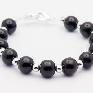 May include: A black beaded bracelet with silver spacers. The bracelet is made of round, black beads and silver metal spacers.