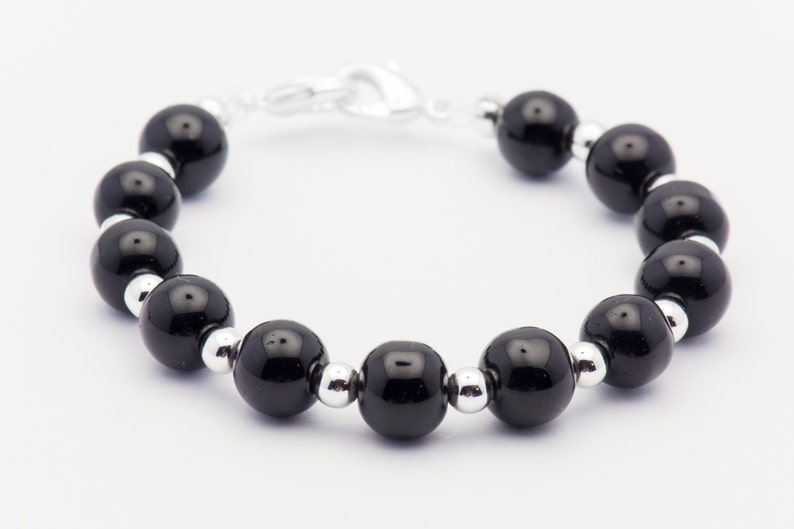 May include: A black beaded bracelet with silver spacers. The bracelet is made of round, black beads and silver metal spacers.