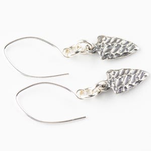 K&ouml;nnte beinhalten: Ein Paar silberne Ohrringe mit einem strukturierten Pfeilspitzen-Design. Die Ohrringe sind aus Sterlingsilber gefertigt und haben ein schlichtes, elegantes Design.