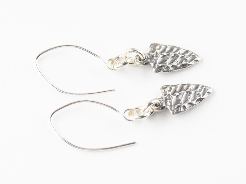 K&ouml;nnte beinhalten: Ein Paar silberne Ohrringe mit einem strukturierten Pfeilspitzen-Design. Die Ohrringe sind aus Sterlingsilber gefertigt und haben ein schlichtes, elegantes Design.