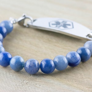 May include: A blue gemstone beaded bracelet with a silver medical ID tag. The tag has a red medical symbol.