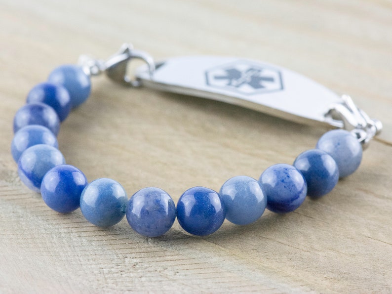 May include: A blue gemstone beaded bracelet with a silver medical ID tag. The tag has a red medical symbol.