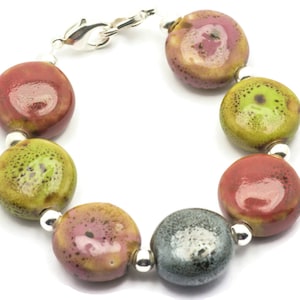 May include: A bracelet made of round, colourful ceramic beads with a silver clasp. The beads are in shades of red, green, pink, and grey.