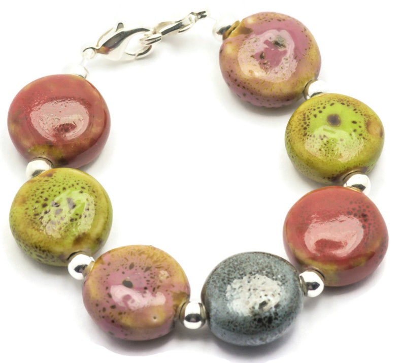 May include: A bracelet made of round, colourful ceramic beads with a silver clasp. The beads are in shades of red, green, pink, and grey.
