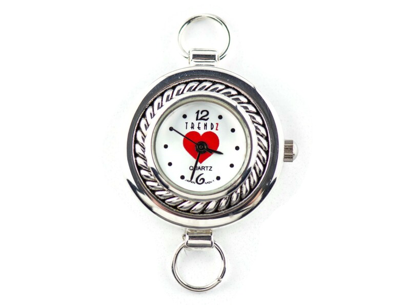 May include: Silver pocket watch with a white face, a red heart, and the word "TRENDZ". The watch has a decorative rope-like border and two ring attachments.