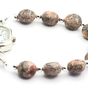 May include: A silver watch with a square face and a brown and white speckled stone bracelet.