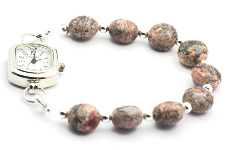 May include: A silver watch with a square face and a brown and white speckled stone bracelet.
