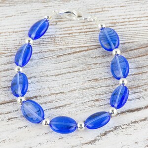 May include: A blue glass bead bracelet with silver accents. The bracelet is made of oval-shaped beads and has a silver clasp.
