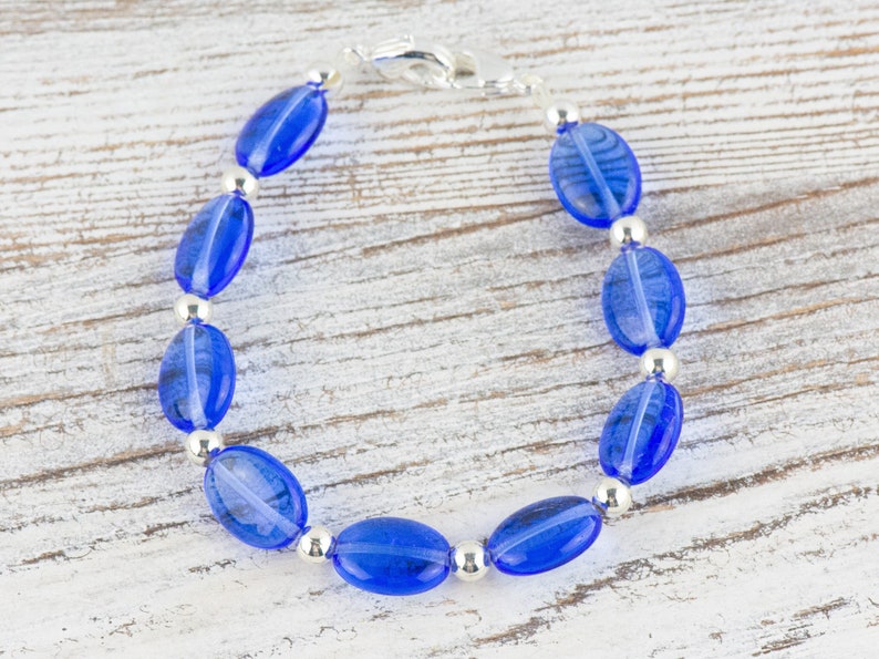 May include: A blue glass bead bracelet with silver accents. The bracelet is made of oval-shaped beads and has a silver clasp.