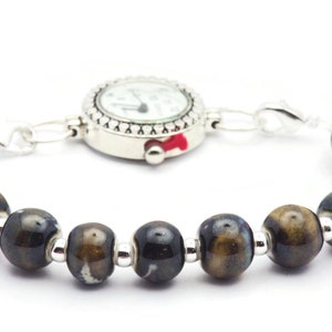 May include: A silver watch with a white face and black hands is attached to a bracelet made of brown and black ceramic beads.