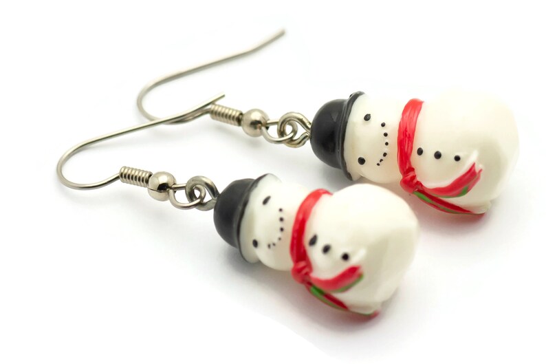 May include: A pair of silver snowman earrings with red and green accents. The snowmen are white with black hats and black eyes.
