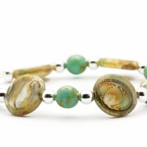 Op de afbeelding: Een armband met afwisselende turquoise en bruine glazen kralen, gescheiden door zilveren kralen.