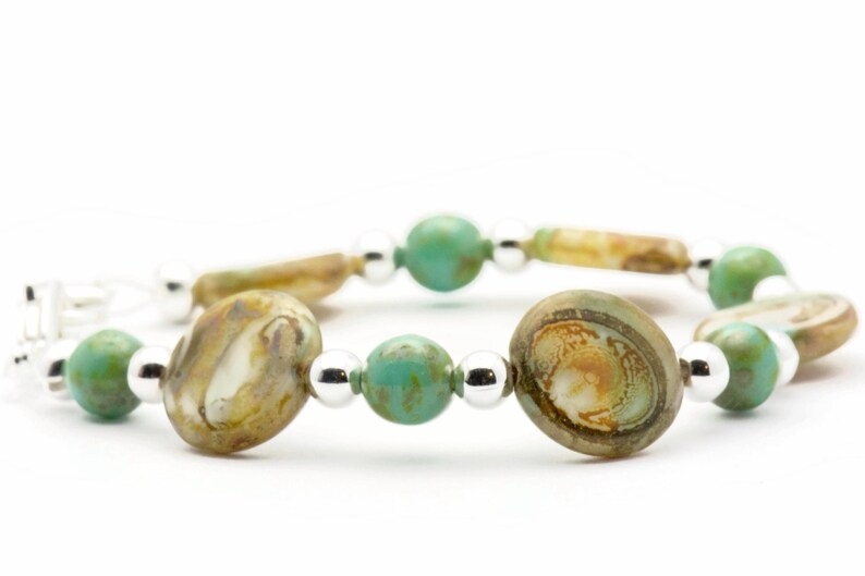 Op de afbeelding: Een armband met afwisselende turquoise en bruine glazen kralen, gescheiden door zilveren kralen.