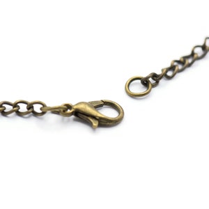 May include: A close-up of a gold-toned chain necklace with a lobster clasp closure. The chain is made of small, linked metal pieces.
