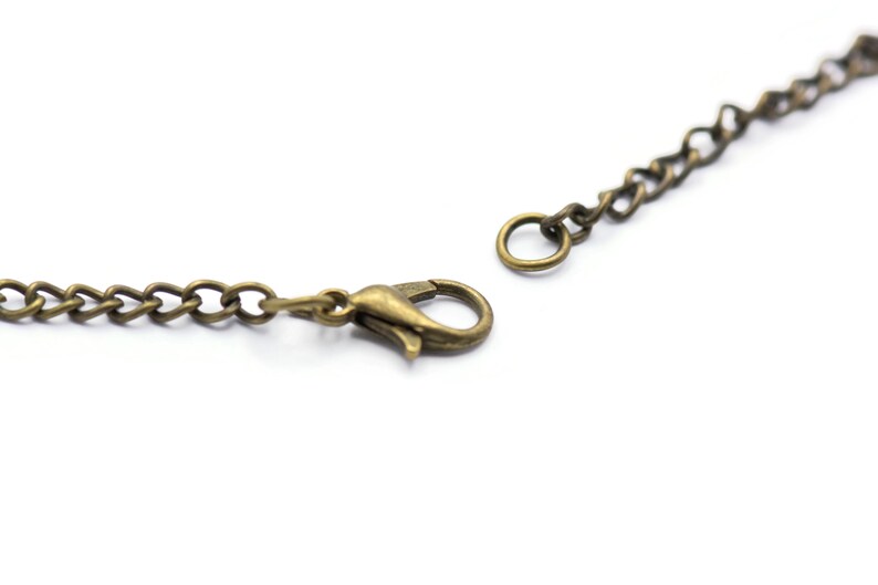 May include: A close-up of a gold-toned chain necklace with a lobster clasp closure. The chain is made of small, linked metal pieces.
