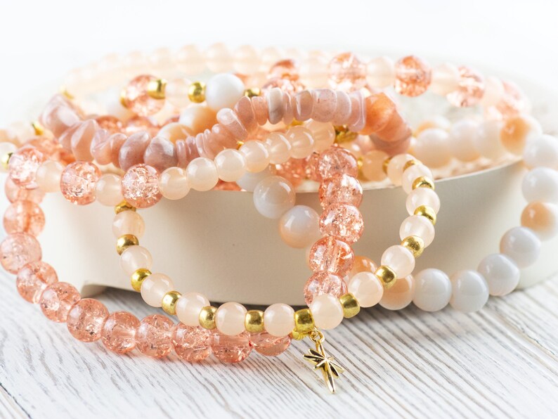 May include: A set of pink and gold beaded bracelets with a star charm. The bracelets are made of different types of beads, including sunstone, glass, and gold.