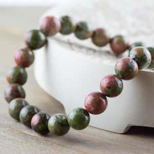 May include: A green and pink gemstone bracelet with round beads. The bracelet is made of natural stones and is approximately 7 inches in length.