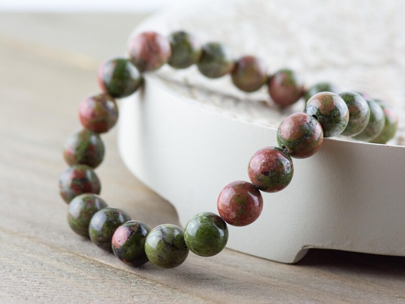 May include: A green and pink gemstone bracelet with round beads. The bracelet is made of natural stones and is approximately 7 inches in length.