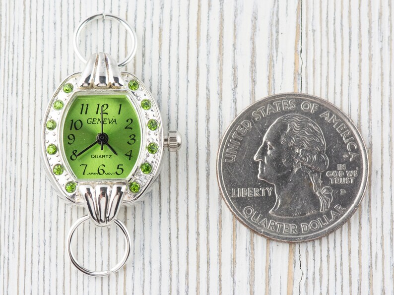 Op de afbeelding: Een zilveren horloge met een groene wijzerplaat en strass-accenten. Het horloge is ongeveer zo groot als een Amerikaanse kwart.