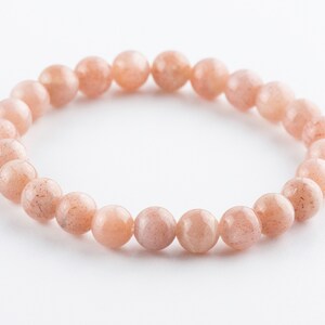 May include: A bracelet made of light pink sunstone beads. The beads are round and have a slightly textured surface.