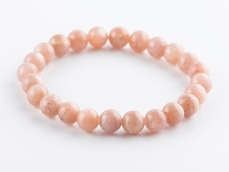 May include: A bracelet made of light pink sunstone beads. The beads are round and have a slightly textured surface.