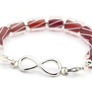 K&ouml;nnte beinhalten: Ein Armband aus roten und wei&szlig;en Glasperlen mit einem Unendlichkeits-Anh&auml;nger. Das Armband ist aus Silber und hat einen Verschluss.