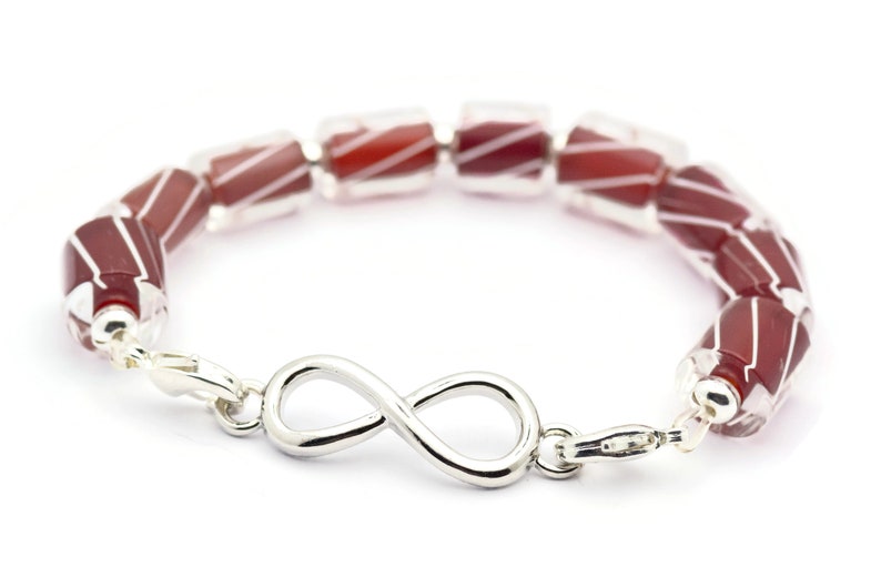 K&ouml;nnte beinhalten: Ein Armband aus roten und wei&szlig;en Glasperlen mit einem Unendlichkeits-Anh&auml;nger. Das Armband ist aus Silber und hat einen Verschluss.