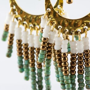 May include: Gold hoop earrings with a fringe of turquoise, gold, and white beads.