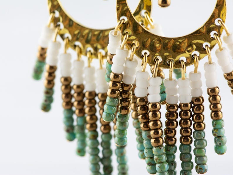 May include: Gold hoop earrings with a fringe of turquoise, gold, and white beads.