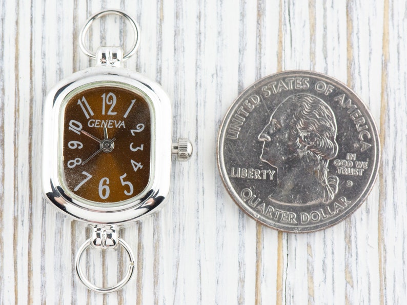 May include: A silver Geneva watch with a brown face and white numerals, next to a U.S. quarter. The watch has a rectangular face with rounded corners and a small crown. The quarter shows a profile of George Washington.