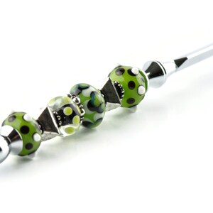 May include: A silver pen with a green and white patterned bead handle.