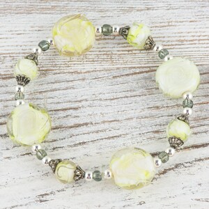 Peut inclure: Un bracelet de perles en verre blanc et vert avec des accents argent&eacute;s. Les perles sont rondes et ont un motif en spirale.